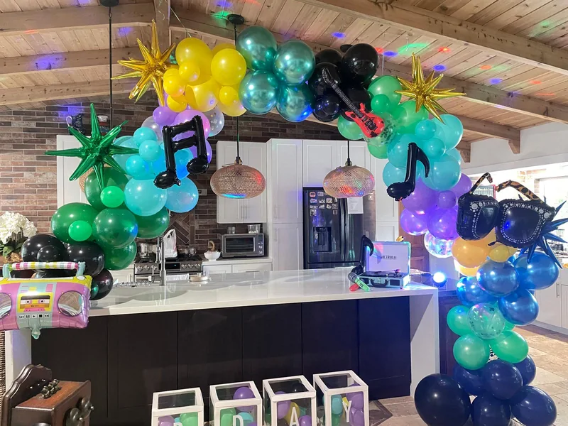 A multicolor balloon arch with musical notes, a guitar, starburst balloons and a boombox prop.